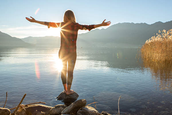 女人站在岩石附近美丽的高山湖泊外展双臂。