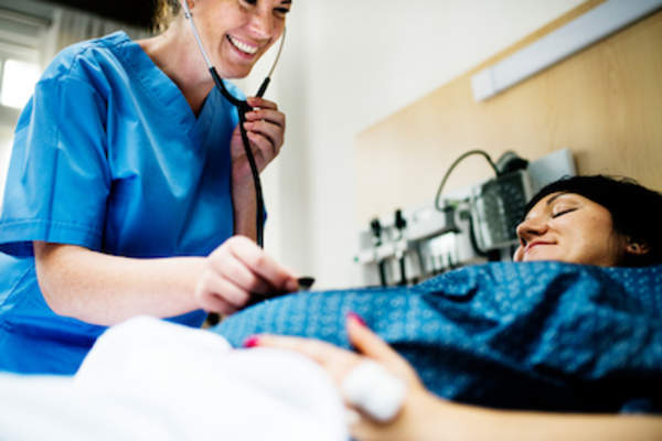 护士用听诊器在孕妇肚子上听婴儿的心跳。