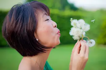 一位资深女士在吹蒲公英的种子