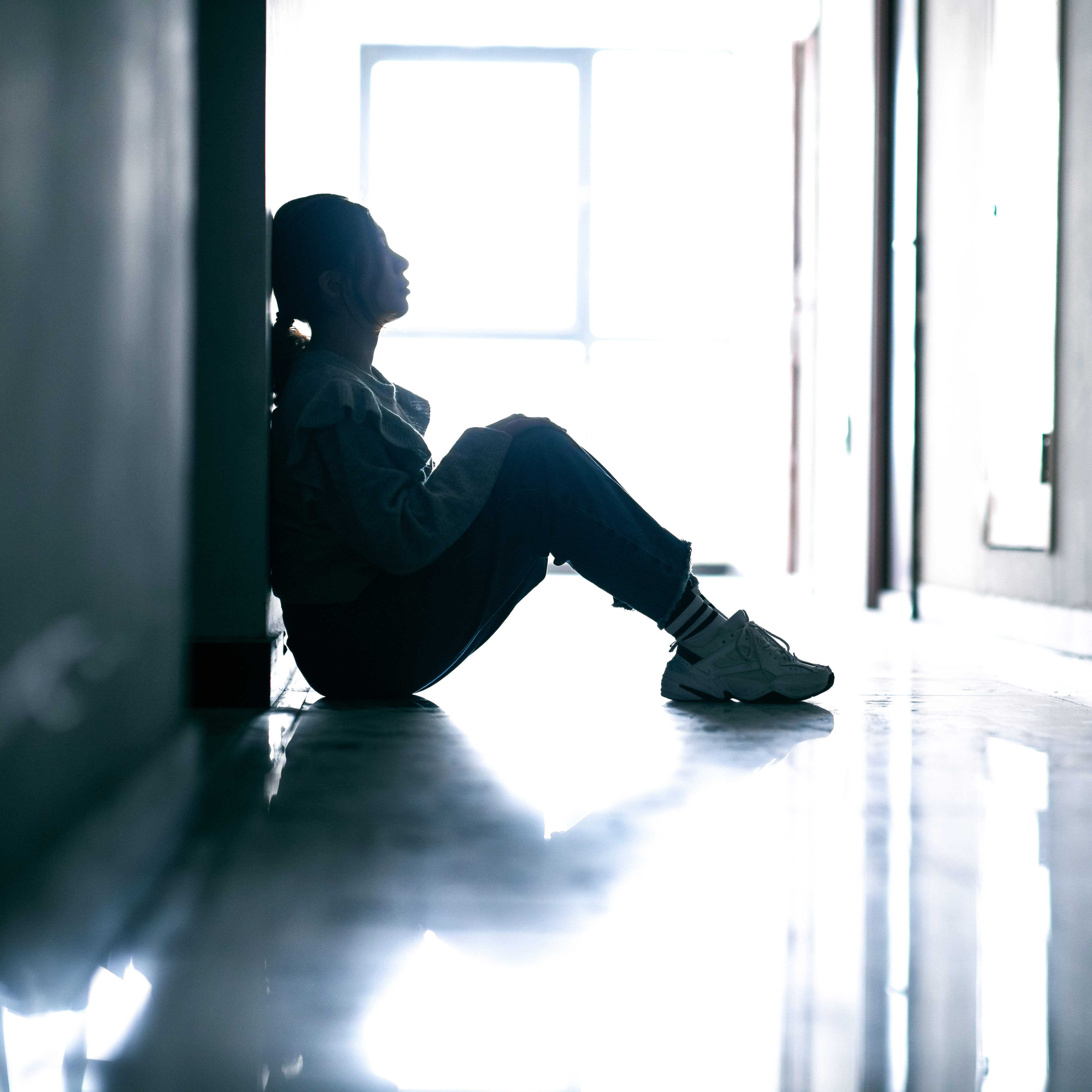 一个悲伤的女人坐在地板上的剪影。