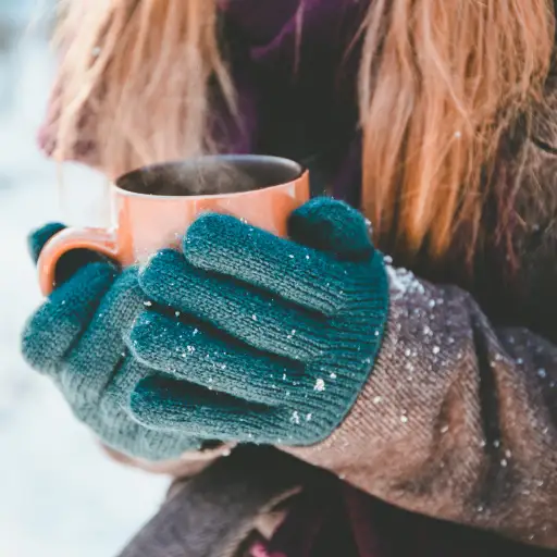 Woman outside holding mug and wearing winter gloves