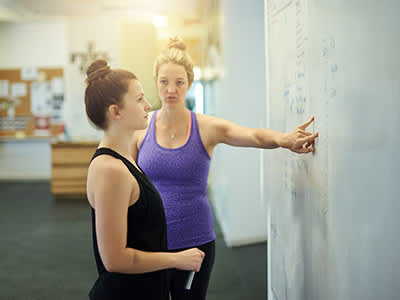 一个女人和她的教练看在白板上的锻炼计划。