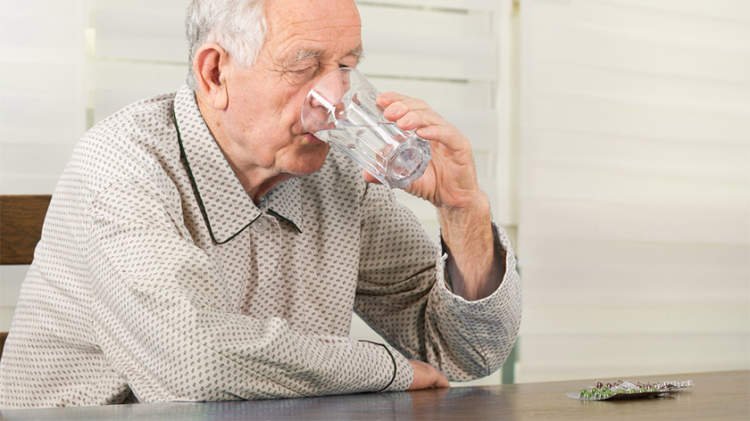 一位老人正在用一杯水服药。