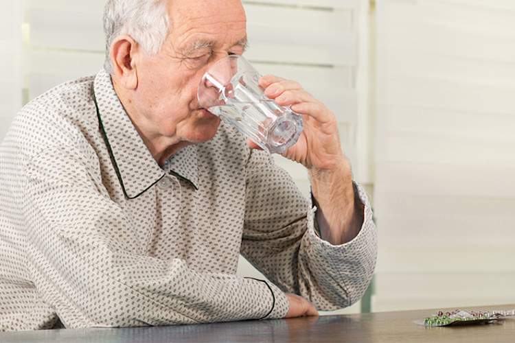 一位老人正在用一杯水服药。