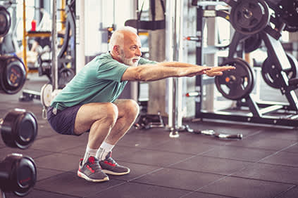 老人做蹲在健身房。