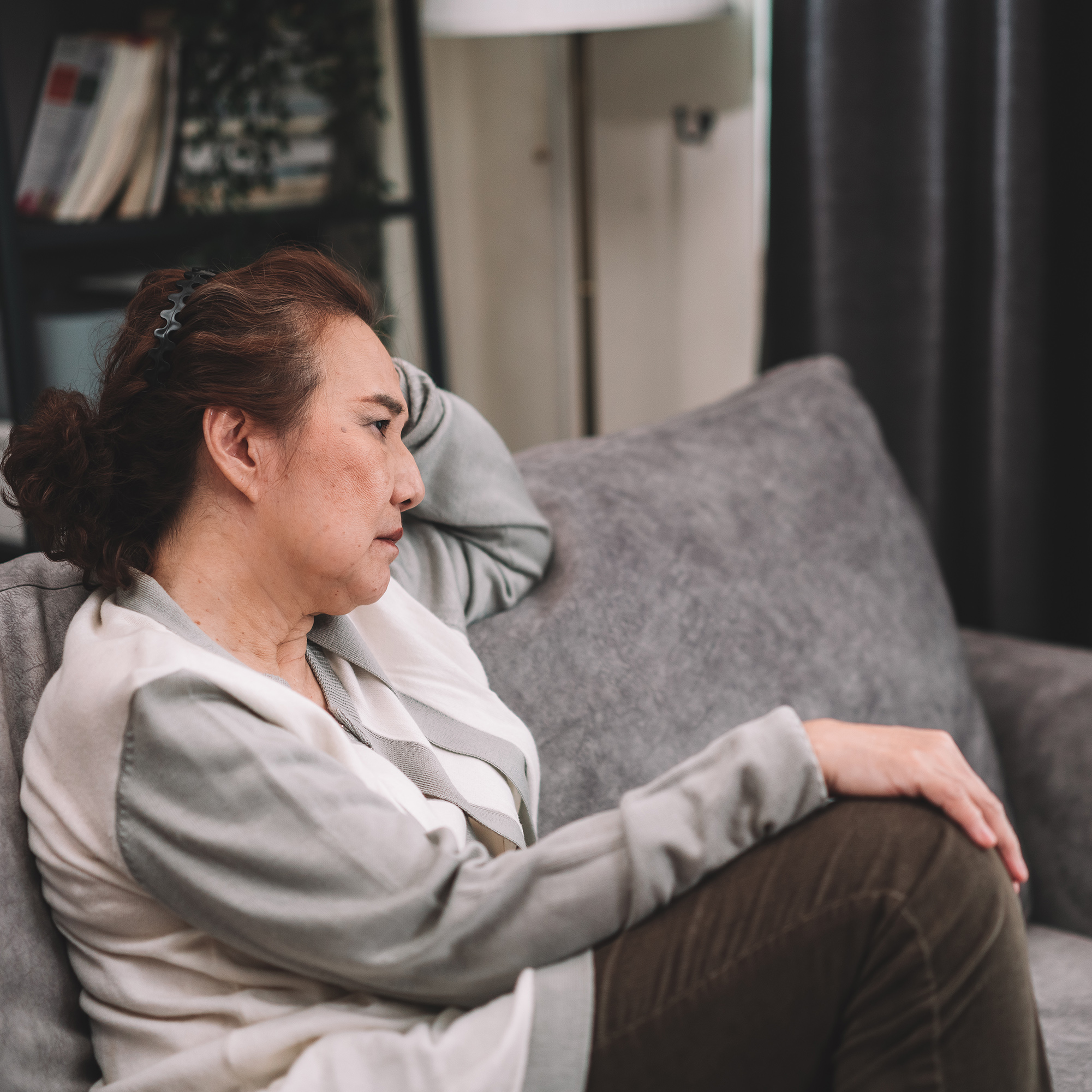 一位老妇人坐在家里的沙发上，对自己的生活忧心忡忡。