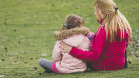 母亲和小女儿坐在公园的草地上。
