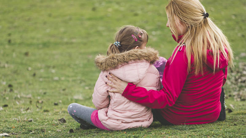 妈妈和小女儿坐在公园的草地上。