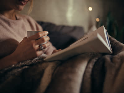 女人在沙发上看书，手里拿着咖啡。