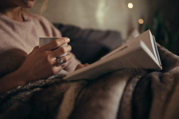 女人在沙发上看书,手里拿着咖啡。