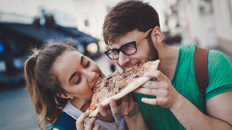 快乐的年轻夫妇在街上分享比萨饼。