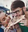 在街道上分享切片薄饼的愉快的年轻夫妇。