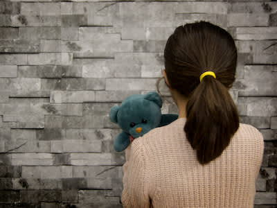 创伤的孩子抱着玩具熊的脸砖墙。
