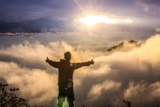 日出时站在悬崖上竖起两个大拇指的快乐男人