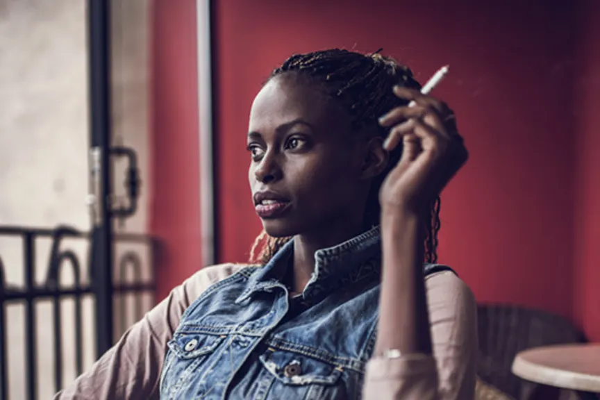 年轻黑人妇女在大阳台的抽烟的香烟。