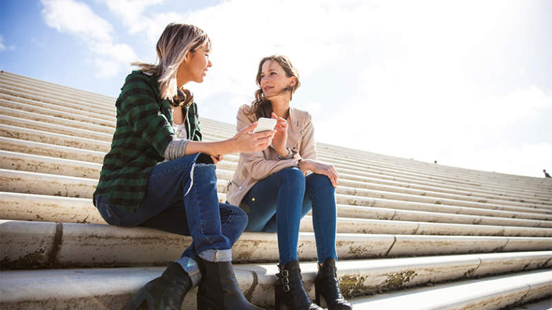 两个年轻女人坐在楼梯上聊天，喝着咖啡。