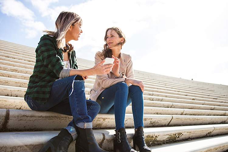 两名年轻妇女坐在楼梯上聊天和喝咖啡。