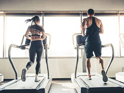 男人和女人在健身房的跑步机上并排跑步。