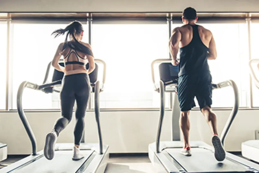 男人和女人在健身房的跑步机上并肩跑步。