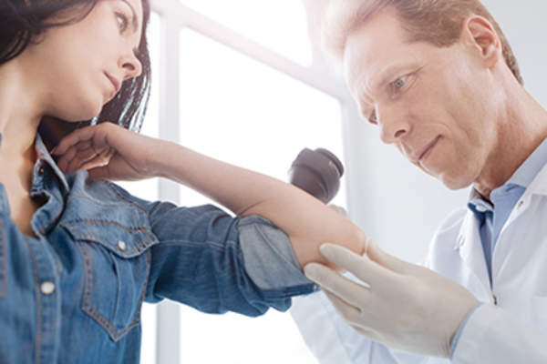 Scrupulous senior doctor using dermatoscope for skin examination at work