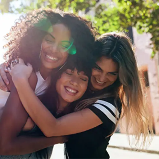 三个年轻的女性朋友，微笑着拥抱着。