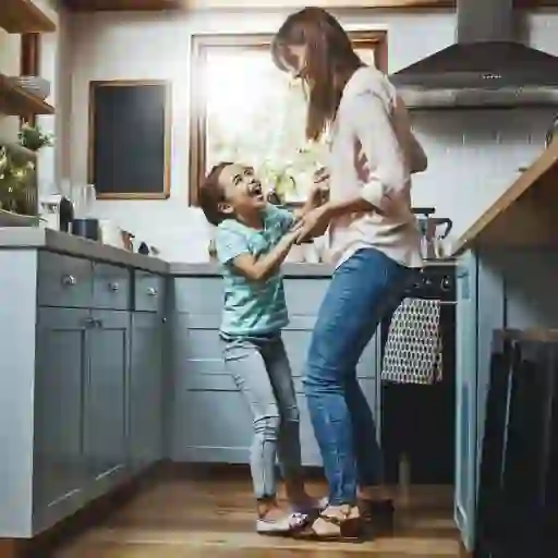 一位母亲和年幼的女儿微笑着在厨房里跳舞。