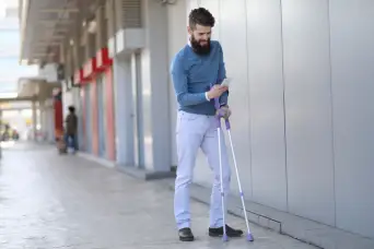 young bearded man with arm crutches texting