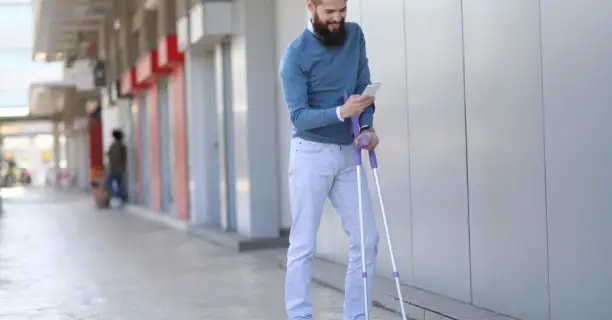 young bearded man with arm crutches texting