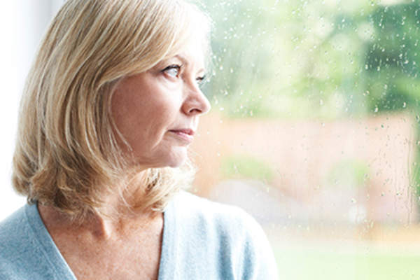 悲伤的成年妇女,患有广场恐惧症,望着窗外