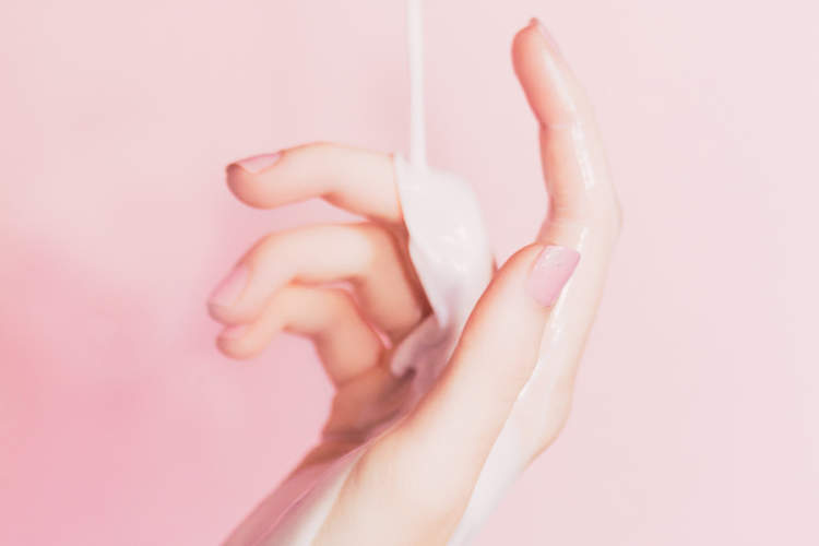 手放在粉色的背景上，使其达到乳液的倾倒