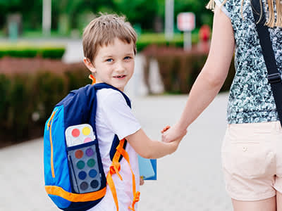 孩子穿着一个背包走路上学与他的妈妈。