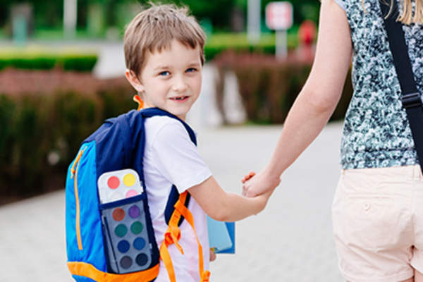 孩子穿着一个背包走路上学与他的妈妈。