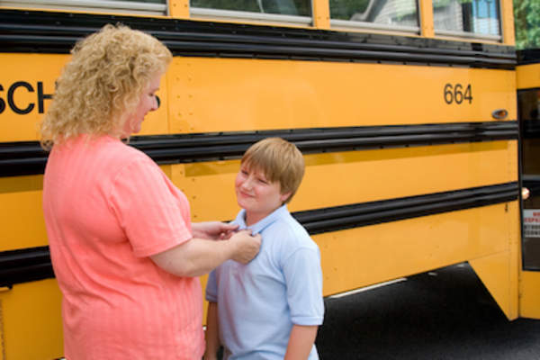 母亲在孩子上校车前把衬衫扣好。