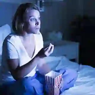Woman staying up late and eating popcorn in bed.