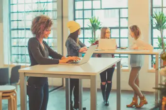 Women using standing desks in an office.