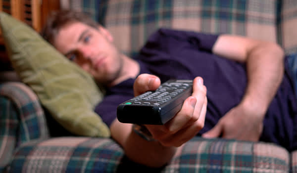 男人躺在沙发上，手里拿着遥控器狂看电视。