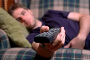 一名男子躺在沙发上，手里拿着遥控器，疯狂地看电视。