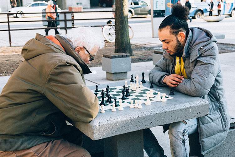 Young man and old man playing chess in the park