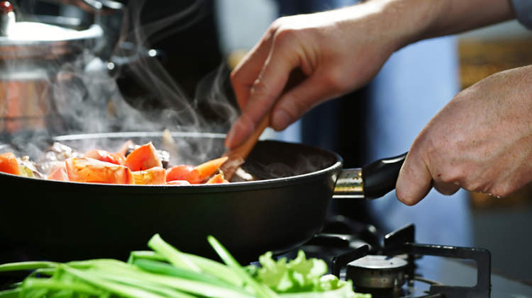 一只手拿着木勺在炉子上的煎锅搅拌食物。