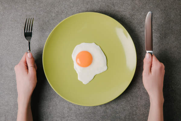 单只鸡蛋放在盘子里，手拿刀叉却不吃