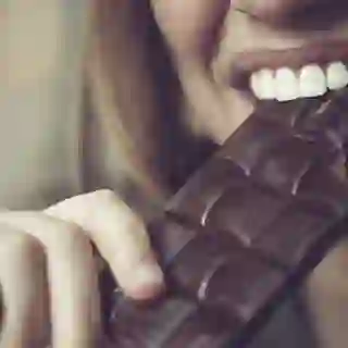 Woman eating a bar of dark chocolate.