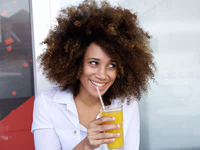 微笑的女人用吸管喝果汁。