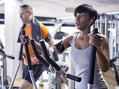年轻女子和男子在健身房椭圆锻炼。