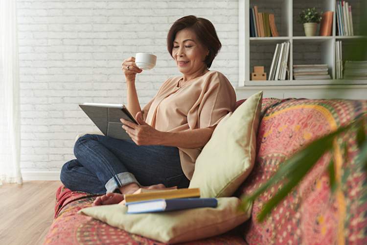 Woman drinking tea and reading on couch at home.