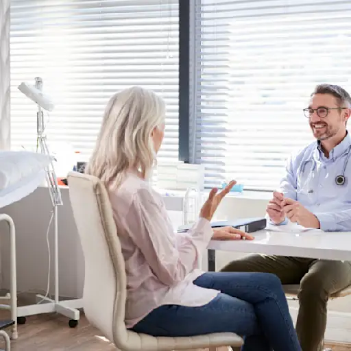 Mature Female Patient In Consultation With Doctor Sitting At Desk In Office