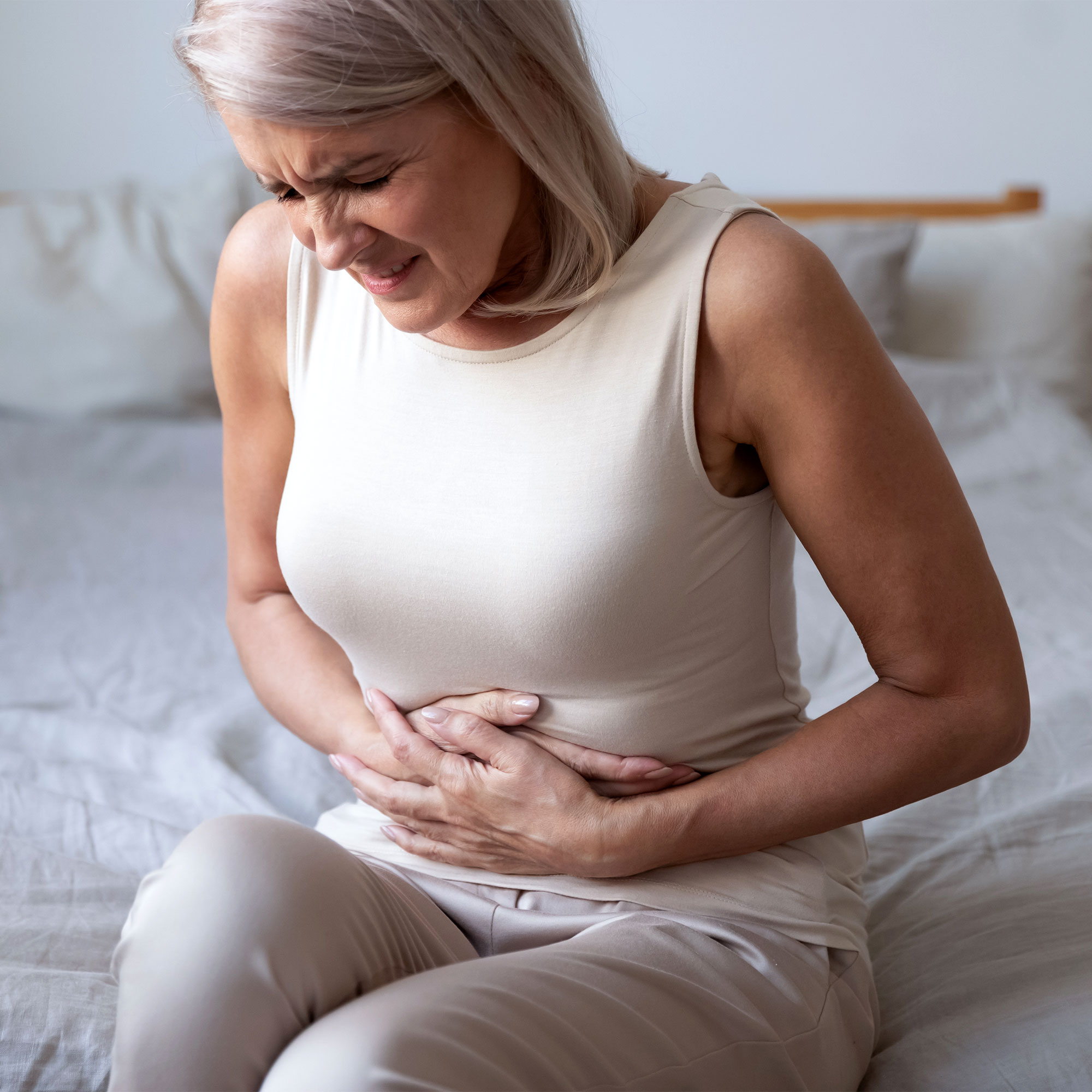 一个女人坐在床上，摸着她疼痛的肚子