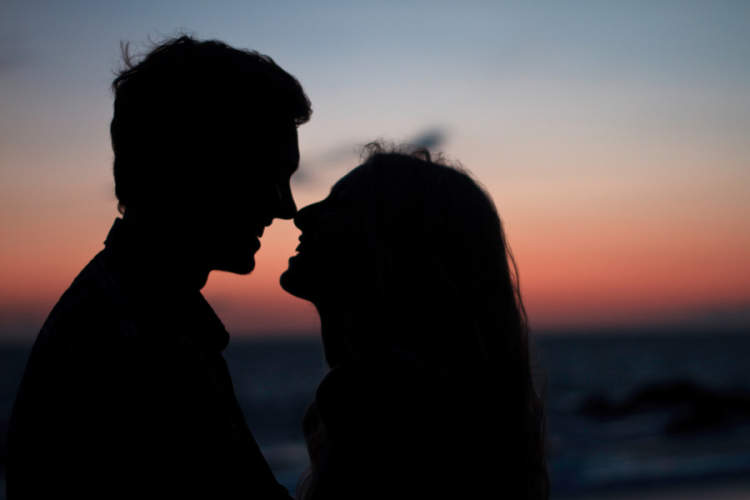 一对情侣在夕阳下亲吻和微笑的剪影