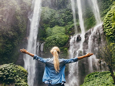 一个女人高举双手站在瀑布旁。