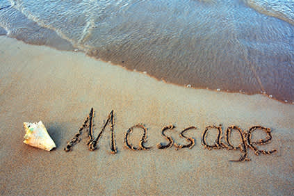 文字按摩写在海滩旁边的贝壳和波浪。