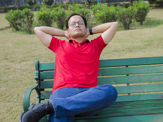 一个男人坐在长凳上思考，双手放在脑后。